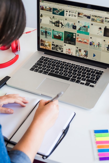 Mujer tomando notas cerca de laptop y auriculares en mesa