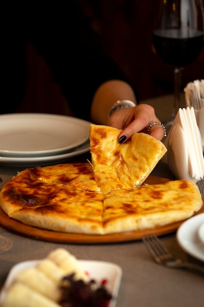 mujer tomando una rebanada de pan de queso georgiano khachapuri