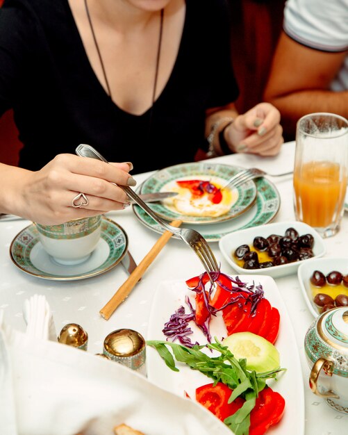 Mujer tomando rodaja de tomate servido para el desayuno