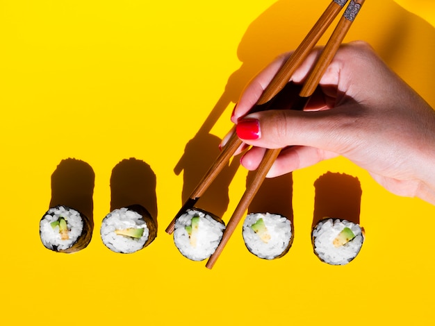 Mujer tomando un rollo nigiri de una mesa amarilla