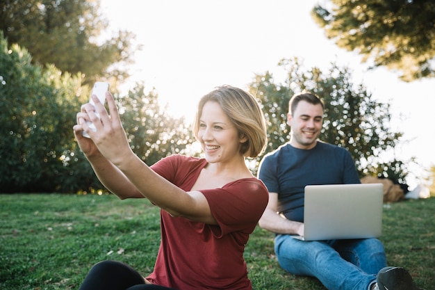 Mujer tomando selfie cerca de hombre con laptop
