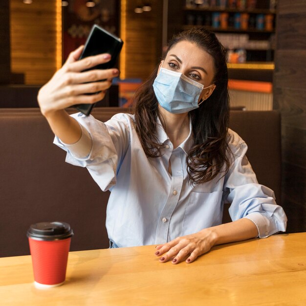 Mujer tomando un selfie en un restaurante mientras usa una máscara médica