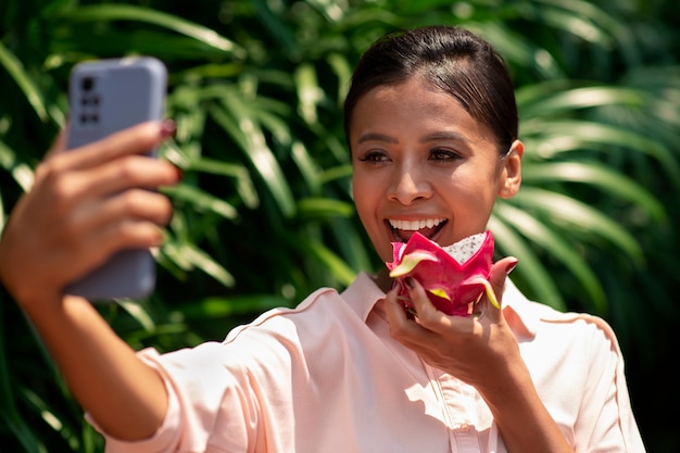 Foto gratuita mujer tomando selfie con teléfono inteligente mientras come fruta de dragón