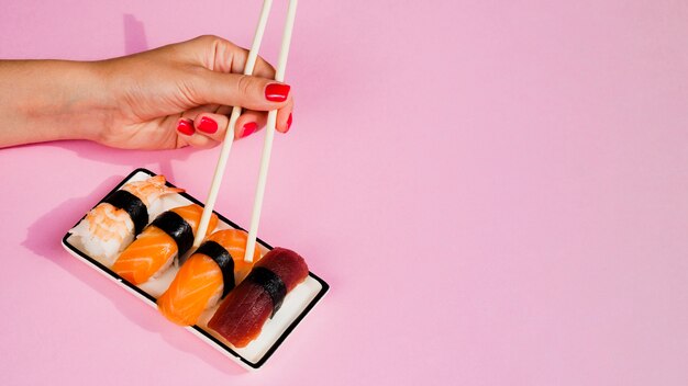 Mujer tomando un sushi paz con palillos de placa