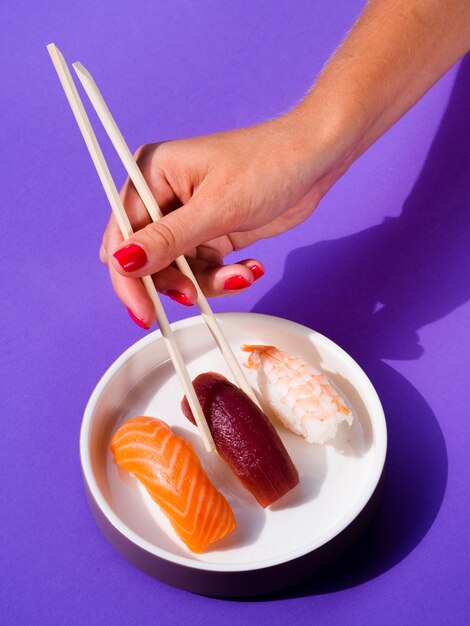 Mujer tomando un sushi del plato de sushi con palillos