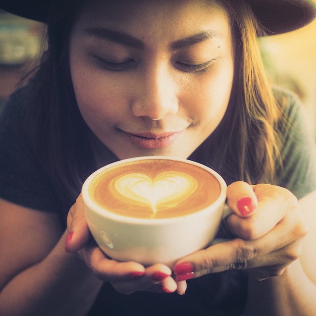 Mujer tomando una taza de café con un corazón dibujado en la espuma