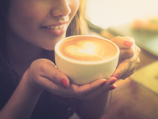 Mujer tomando una taza de café con un corazón dibujado en la espuma