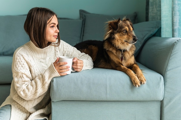 Mujer tomando una taza de café junto a su perro en casa durante la pandemia