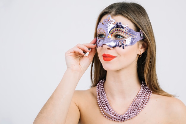 Mujer en topless en máscara de carnaval con collar de perlas sobre fondo blanco