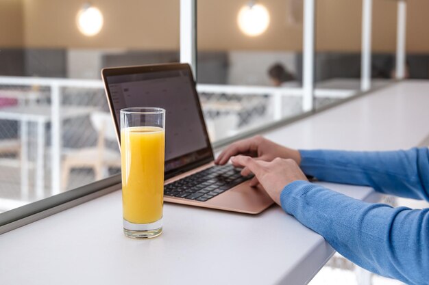 Una mujer trabaja en una computadora portátil en un café bebe jugo de naranja