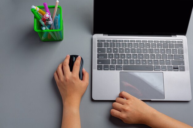 La mujer trabaja con una computadora portátil en casa y sostiene un mouse de computadora en su mano izquierda.