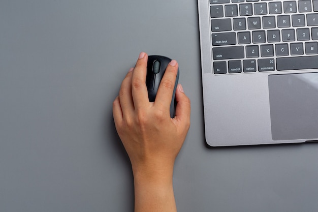 La mujer trabaja con una computadora portátil en casa y sostiene un mouse de computadora en su mano izquierda.