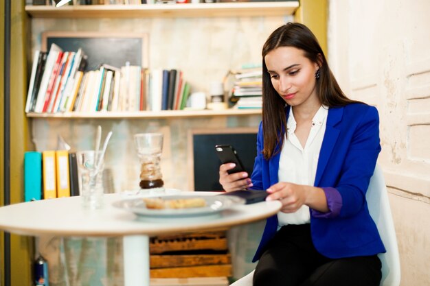 Mujer trabaja con un teléfono inteligente en la mesa en un café