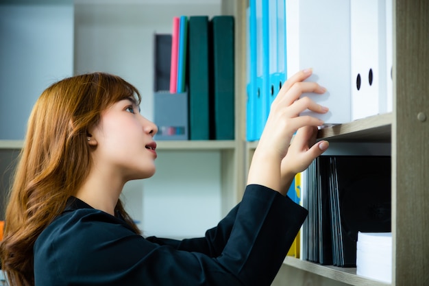 Mujer trabajadora buscando libros de estantes en la biblioteca