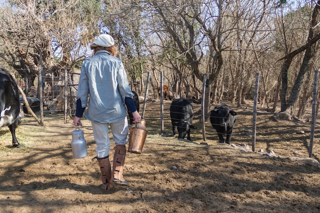 Mujer trabajadora rural caminando en la campiña argentina con latas de leche recién ordeñada