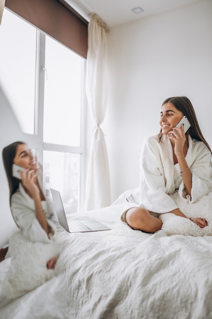 Mujer trabajando en la computadora en la cama y hablando por teléfono