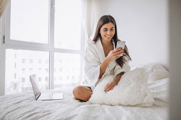 Mujer trabajando en la computadora en la cama y hablando por teléfono