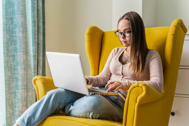 Mujer trabajando en una computadora portátil desde un sillón en casa durante la pandemia