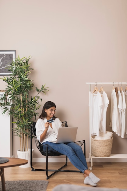 Mujer trabajando en la computadora portátil y sosteniendo una tarjeta en la sala de estar