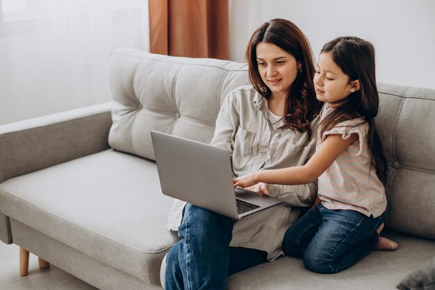 Mujer trabajando en línea en una computadora portátil en casa con su hija
