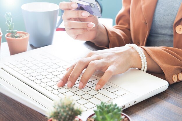 Mujer de trabajo utilizando equipo portátil y la celebración de tarjeta de crédito, compras en línea