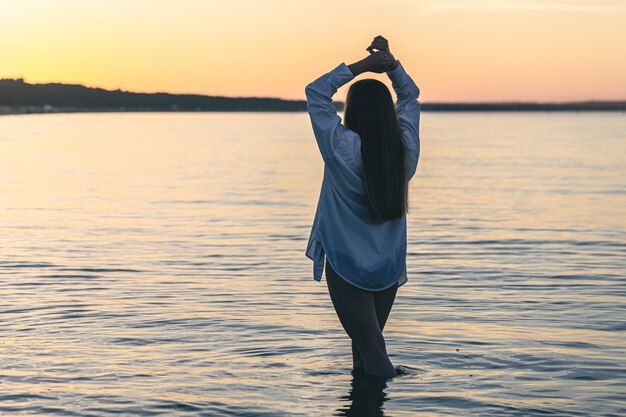 Una mujer en traje de baño y una camisa blanca en el mar al atardecer