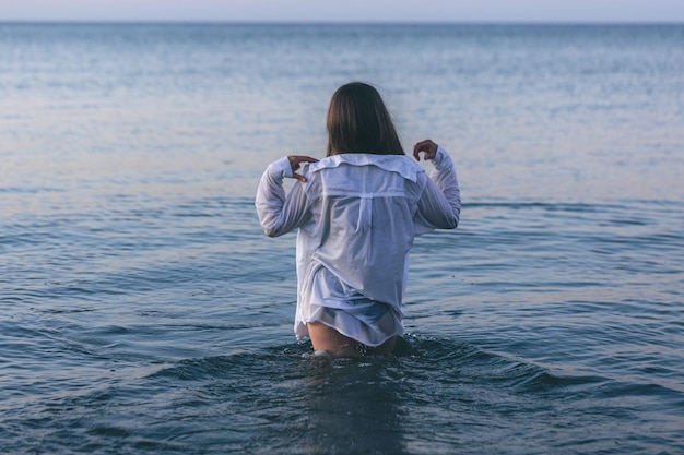 Una mujer en traje de baño y una camisa blanca en el mar.