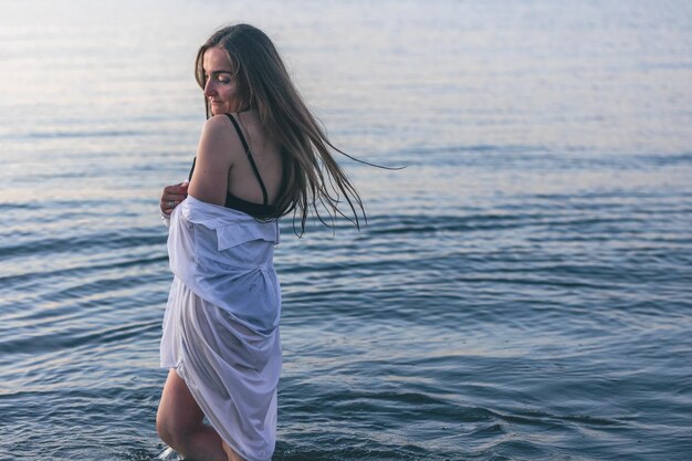 Una mujer en traje de baño y una camisa blanca en el mar.