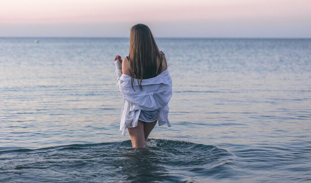 Una mujer en traje de baño y una camisa blanca en el mar.