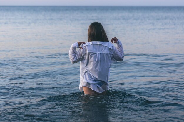 Una mujer en traje de baño y una camisa blanca en el mar.