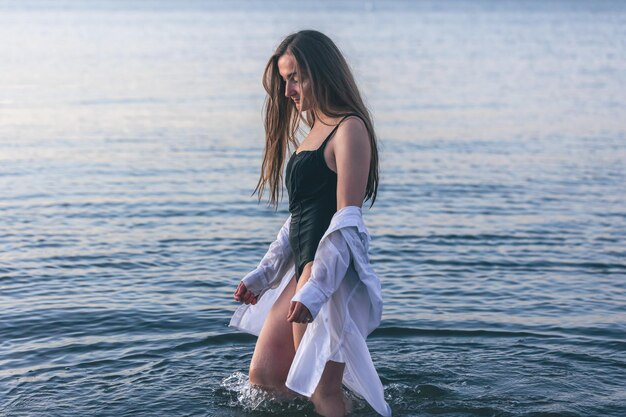 Una mujer en traje de baño y una camisa blanca en el mar.