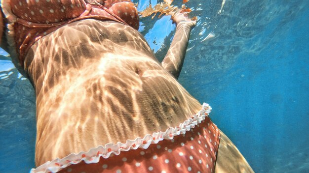 Mujer en traje de baño naranja en el agua azul y transparente del mar Mediterráneo. Sosteniendo la camara