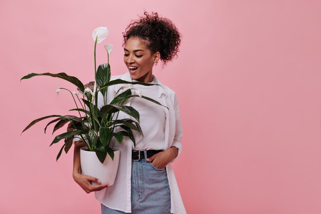 Mujer en traje brillante tiene planta en pared rosa