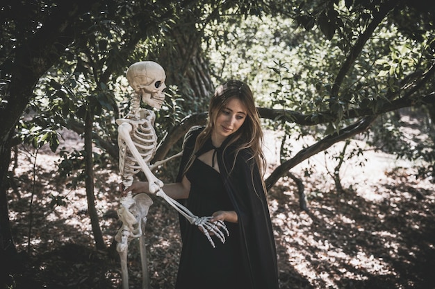 Foto gratuita mujer en traje de bruja con esqueleto y mirando hacia abajo