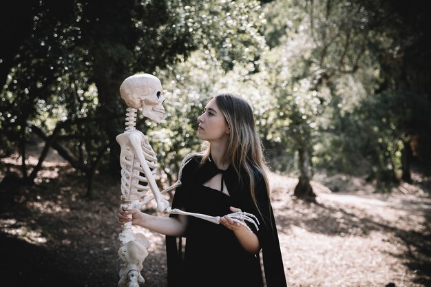 Mujer en traje de bruja mirando atento al esqueleto