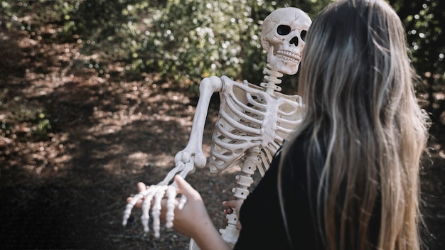 Mujer en traje de bruja que se inclina esqueleto
