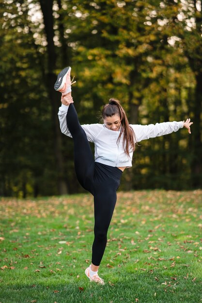 Mujer en traje de deporte en el parque haciendo splits de pie.