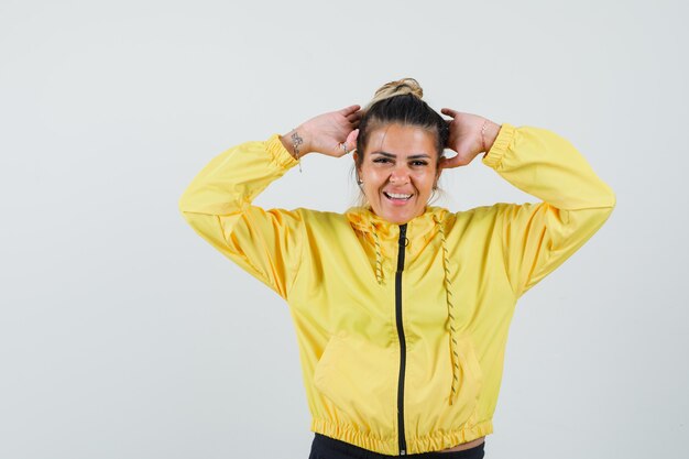 Mujer en traje deportivo cogidos de la mano a la cabeza y mirando alegre, vista frontal.