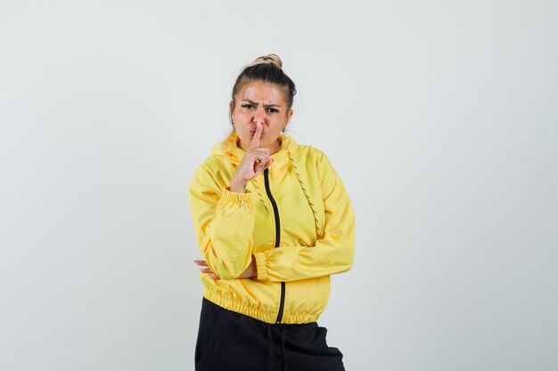 Mujer en traje deportivo mostrando gesto de silencio y mirando serio, vista frontal.