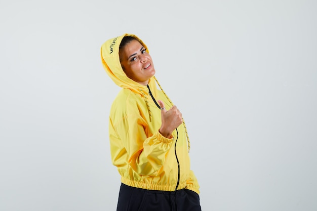 Foto gratuita mujer en traje deportivo posando mientras muestra el pulgar hacia arriba y mira confiada, vista frontal.