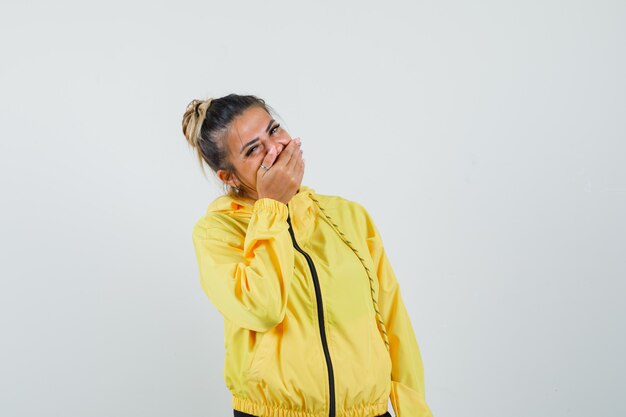 Mujer en traje deportivo sosteniendo la mano en la boca y mirando feliz, vista frontal.