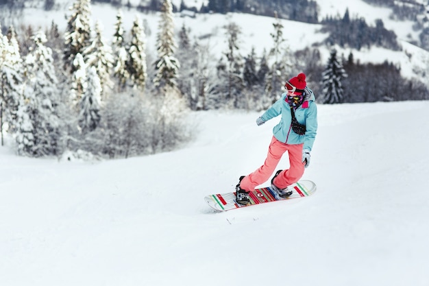 La mujer en traje de esquí mira sobre su hombro bajando la colina en su tabla de snowboard