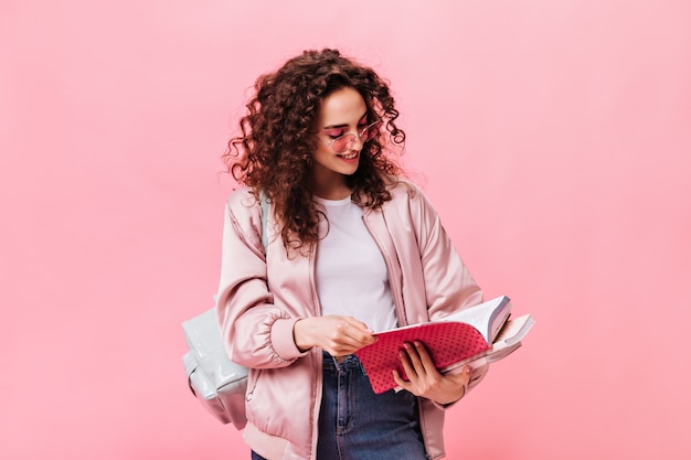 Mujer en traje de luz leer notas en el cuaderno sobre fondo rosa