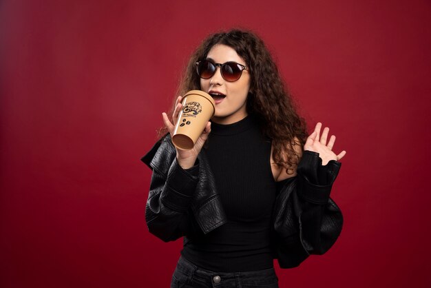 Mujer en traje negro posando con una taza y vasos.