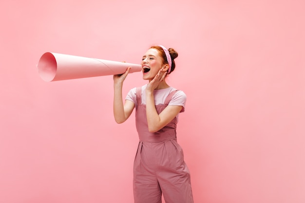 Mujer en traje rosa pegada a su oreja enorme trozo de papel enrollado en tubo.