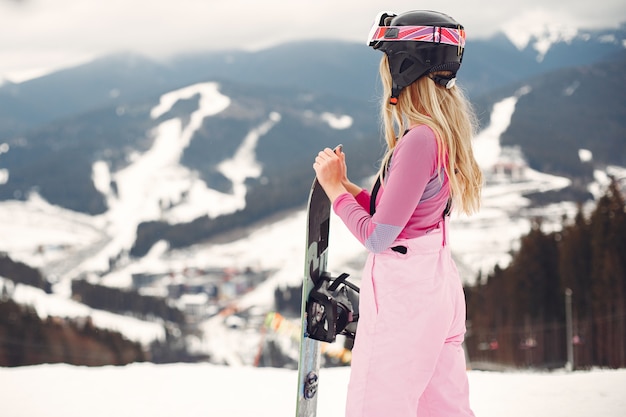 Mujer en traje de snowboard. Deportista en una montaña con una tabla de snowboard en las manos en el horizonte. Concepto de deportes