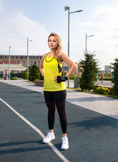 Mujer en trajes deportivos amarillos y negros de pie y posando en una línea de jogging.