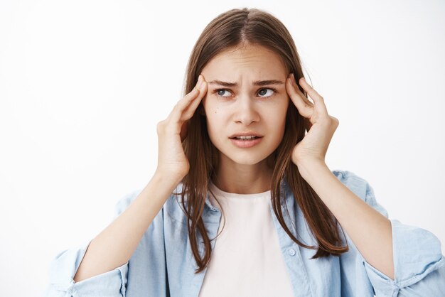 Mujer tratando de pensar y actuar en una situación difícil sosteniendo los dedos en las sienes frunciendo el ceño mirando a un lado teniendo falta de concentración que quiere concentrarse pero sufre dolor de cabeza