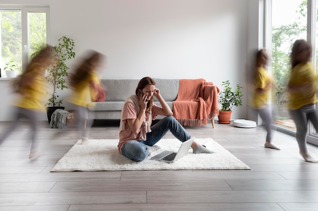 Mujer tratando de trabajar en la computadora portátil desde casa mientras sus hijos corren