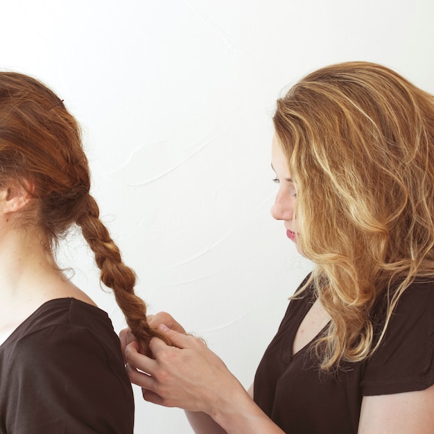 Foto gratuita mujer trenzando el cabello de su hermana contra el telón de fondo blanco